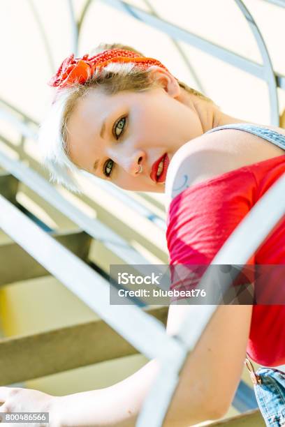 Young Blonde Pinup Girl With A Red Bow On A Emergency Stairway Concept Pinup Woman Stock Photo - Download Image Now