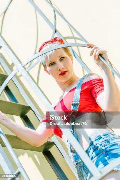 Foto de Jovem Garota Pinup Loira Com Um Laço Vermelho Em Uma Escada De Emergência Mulher Pinup Do Conceito e mais fotos de stock de Adulto