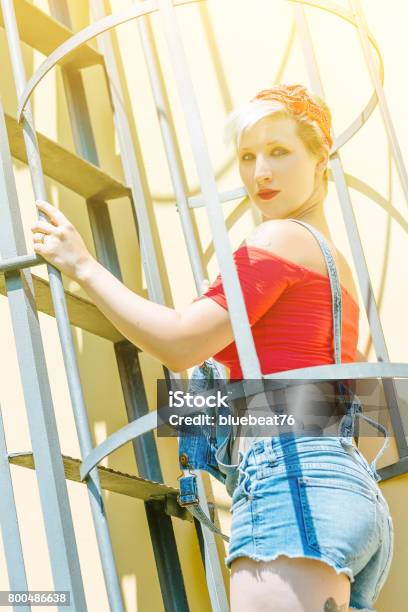 Foto de Jovem Garota Pinup Loira Com Um Laço Vermelho Em Uma Escada De Emergência Mulher Pinup Do Conceito e mais fotos de stock de Adulto