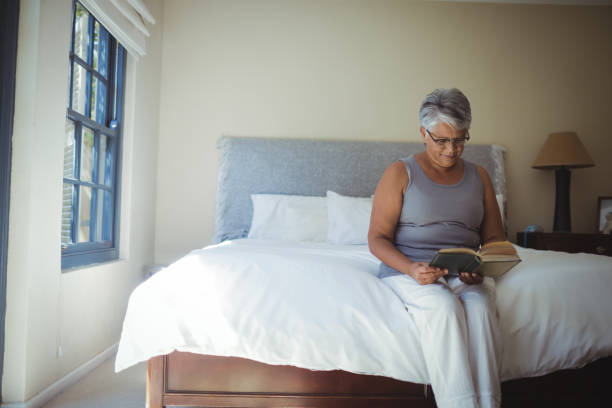 istock Senior woman reading book while sitting on bed in the bed room 800502206