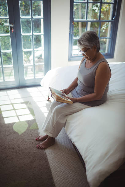 istock Senior woman reading book while sitting on bed in the bed room 800502218