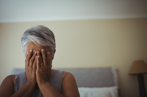 Upset senior woman covering her face at home
