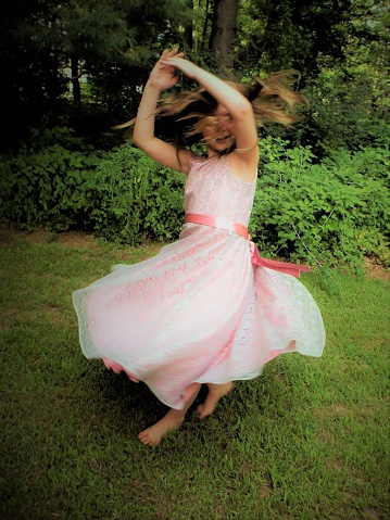 Child outside twirling in pink dress.