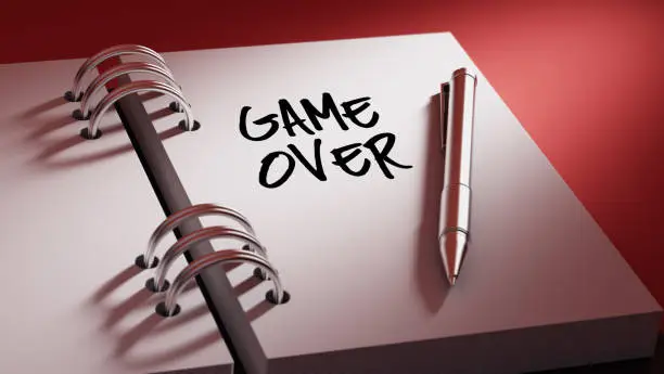 Closeup of a personal agenda setting an important date writing with pen. The words Game over written on a white notebook to remind you an important appointment.