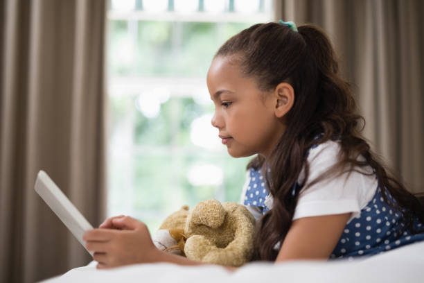 istock Side view of smiling girl using digital tablet while lying on bed 800562252