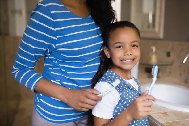 istock Smiling girl with mother brushing teeth in bathroom 800572784