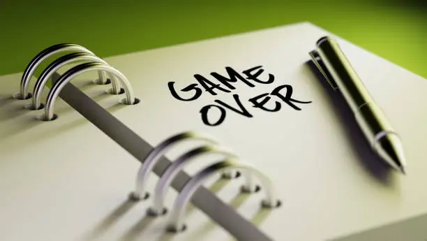 Closeup of a personal agenda setting an important date writing with pen. The words Game over written on a white notebook to remind you an important appointment.