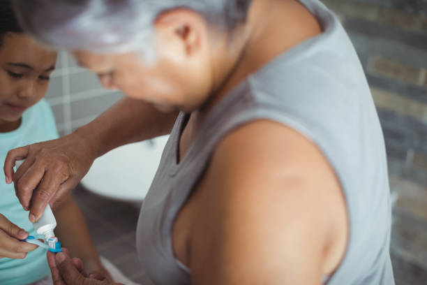 istock Grandmother applying toothpaste on granddaughters brush in the bathroom 800723428
