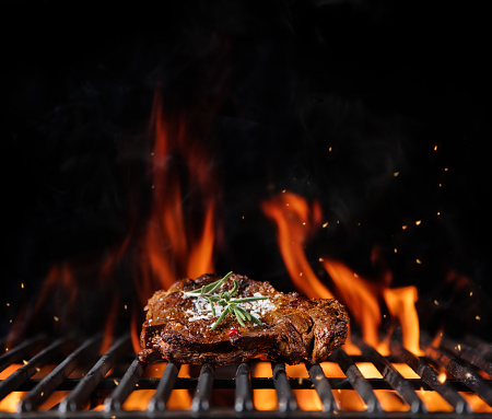 Beef steak on the grill grate, flames on background. Barbecue and grill, delicious food.