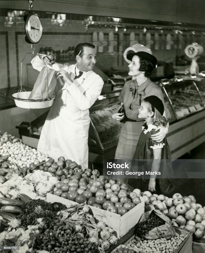 Mother and daughter in supermarket, shop assistant weighing groceries  Old-fashioned Stock Photo