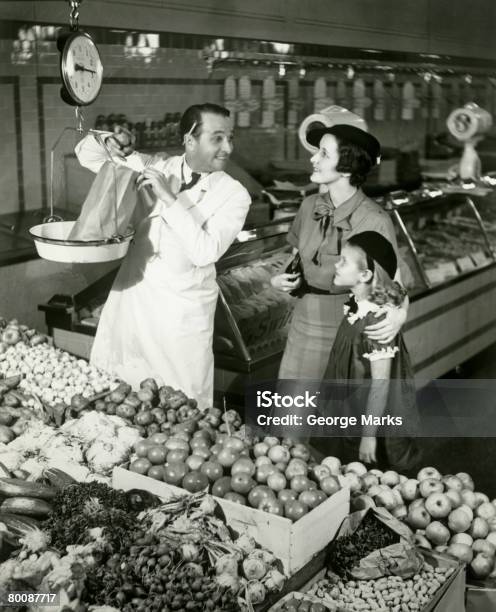 Mother And Daughter In Supermarket Shop Assistant Weighing Groceries Stock Photo - Download Image Now