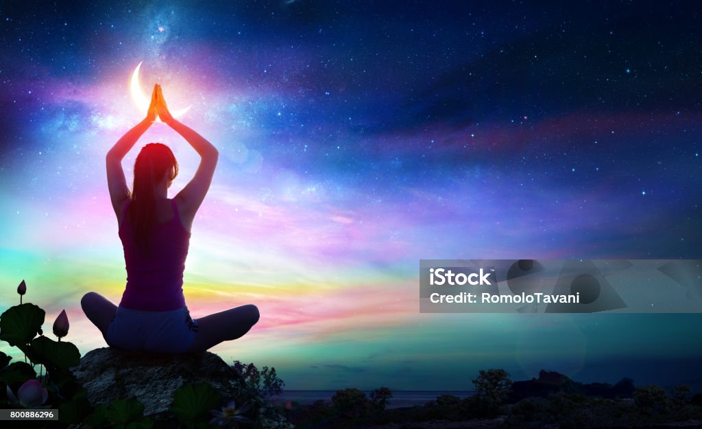 Woman Doing Yoga - Spiritual Contemplation Woman Doing Yoga With Lotus Flowers And Rainbow Gradient In The Sky At Night Chakra Stock Photo