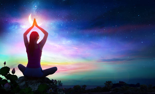 Woman Doing Yoga - Spiritual Contemplation Woman Doing Yoga With Lotus Flowers And Rainbow Gradient In The Sky At Night feng shui photos stock pictures, royalty-free photos & images