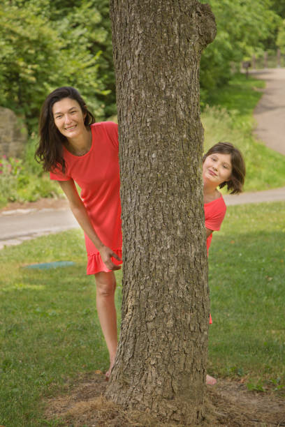 istock mother and daughter peeking out behind a tree 800940644