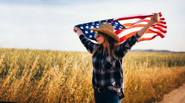 chica alegre país agitando una bandera estadounidense en un campo - cowboy blue meadow horizontal fotografías e imágenes de stock