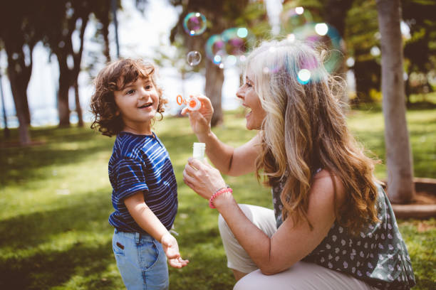 Grandma and grandson laughing and blowing bubbles at the park stock photo