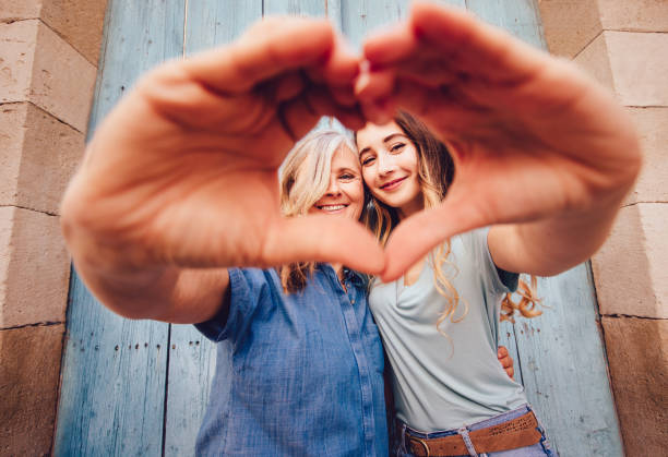 Cheerful grandmother and teenage granddaughter forming a heart shape with their hands in old town