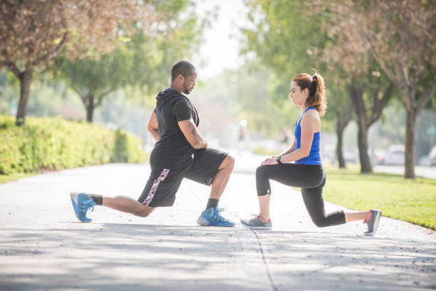 personal trainer doing deep knee bends with client - bending knees imagens e fotografias de stock