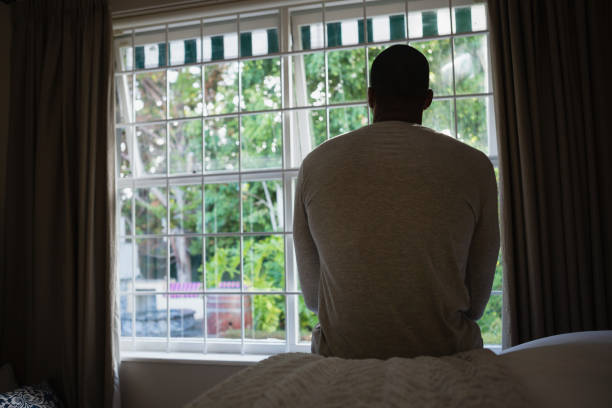 istock Rear view of man sitting on bed against window 800992406