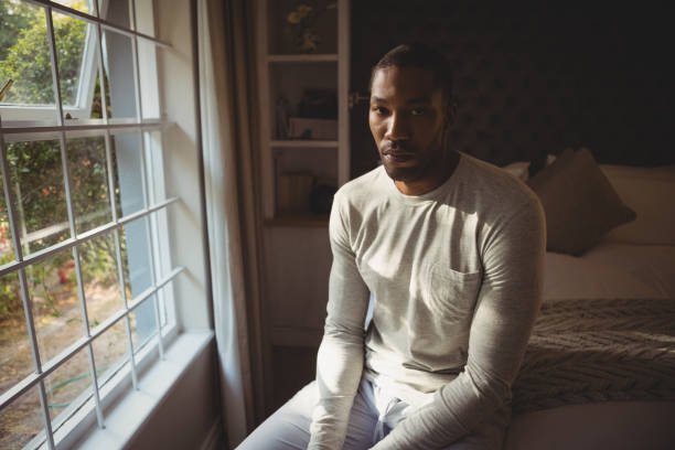 istock Portrait of serious man sitting on bed by window 800992784