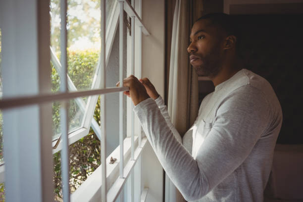 istock Thoughtful man looking out through window at home 800992810