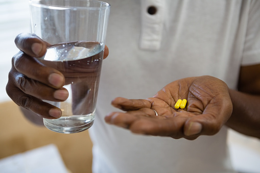 Mid section of senior man holding medicines and drinking water in bathroom at home
