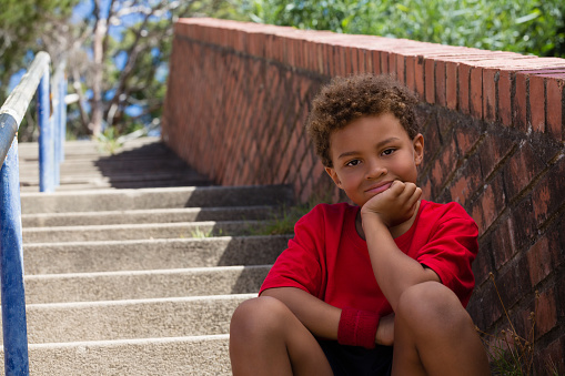 Portrait of boy sitting on staircase in the boot camp on a sunny day