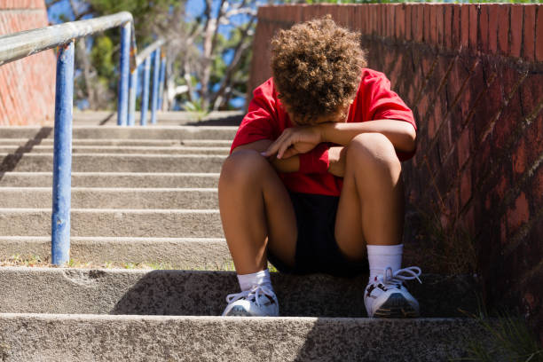 Upset boy sitting on staircase in the boot camp on a sunny day