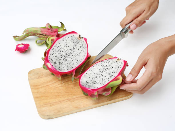 istock Woman hands cutting dragon fruit on chopping board against white background. 801006280