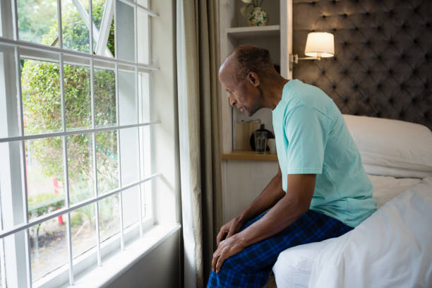 istock Side view of thoughtful senior man sitting on bed by window 801006332