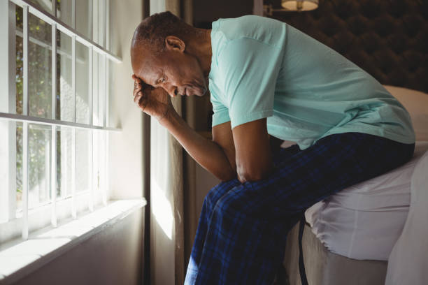 istock Side view of serious senior man sitting on bed by window 801008462