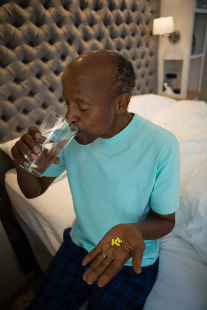 istock Senior man holding medicine while drinking water in bedroom 801008642