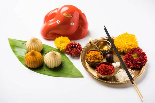 Indian Festival - Indian sweet food called Modak offered as prasad or prashad or chadhava  over green leaf to Lord Ganesha on Ganesh Chaturthi with puja or pooja thali and decorated with flowers