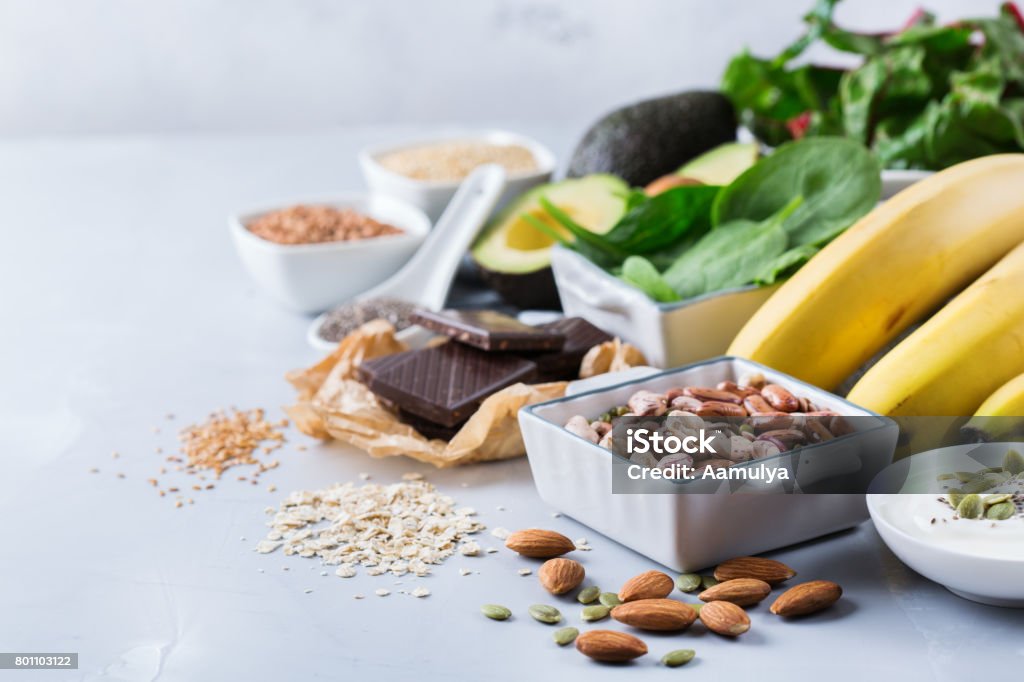 Assortment of healthy high magnesium sources food Healthy food nutrition dieting concept. Assortment of high magnesium sources. Banana chocolate spinach chard, avocado, buckwheat, sesame chia flax seeds, yogurt, nuts, beans oat. Copy space background Magnesium Stock Photo