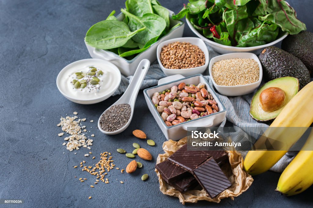 Assortment of healthy high magnesium sources food Healthy food nutrition dieting concept. Assortment of high magnesium sources. Banana chocolate spinach chard, avocado, buckwheat, sesame chia flax seeds, yogurt, nuts, beans oat. Copy space background Magnesium Stock Photo