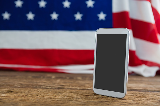 Close-up of American flag and mobile phone arranged on wooden table