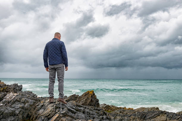 istock Man standing on rocks by the sea overlooking an overcast gloomy sky. 801224584