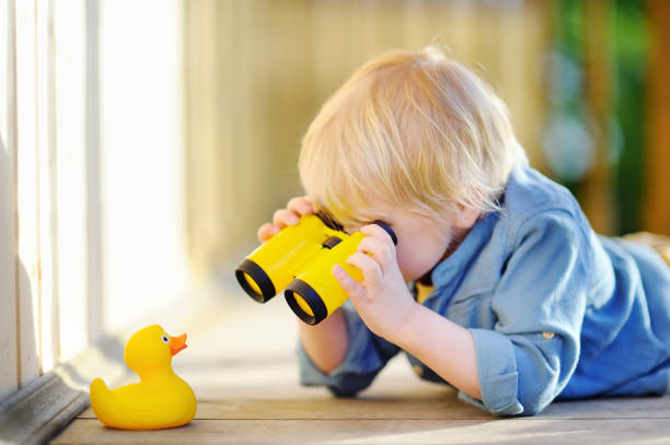 Photo of Cute little boy playing with rubber duck and plastic binoculars outdoors