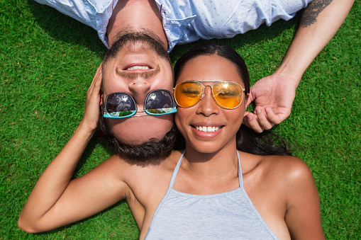 Closeup portrait of smiling young multi-ethnic couple looking at camera and lying on lawn. Top view.
