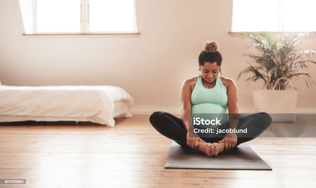 Beautiful expectant mother doing yoga at home Portrait of young pregnant female working out at home. African pregnant woman practicing yoga at home. Prenatal groins stretch. Buddha Konasana Pose. Pregnancy yoga and fitness. Pregnant Stock Photo