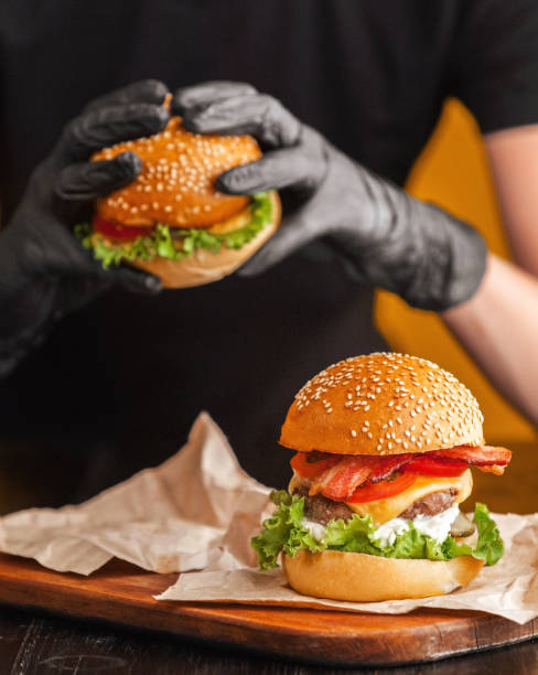 Bright juicy appetizing burgers with a cutlet, cheese, marinated cucumbers, tomatoes and bacon in the hands of a girl, a girl in special gloves for burgers