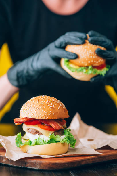 Bright juicy appetizing burgers with a cutlet, cheese, marinated cucumbers, tomatoes and bacon in the hands of a girl, a girl in special gloves for burgers