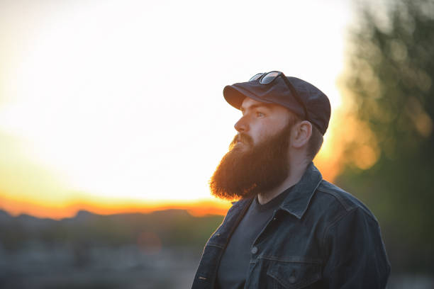 istock Bearded man. A brutal young guy with a large beard in a cap at sunset. 801435448