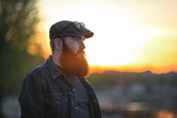 istock Bearded man. A brutal young guy with a large beard in a cap at sunset. 801435450