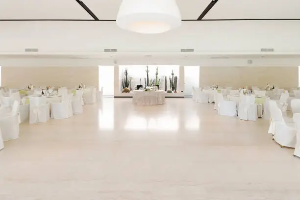 Table of the couple in the middle and tables of guests at the sides in a white room set up for the event to understand a concept of life with love