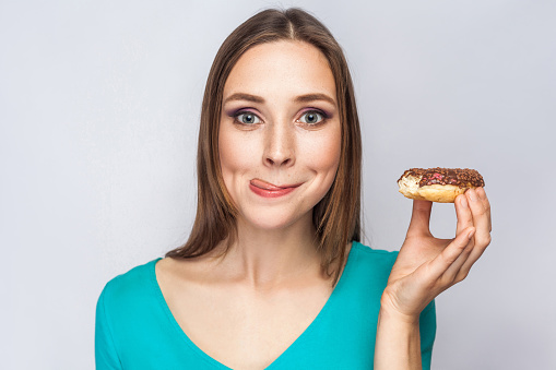 Portrait of beautiful girl with chocolate donuts. enjoing and looking at camera with tongue.  studio shot on light gray background.