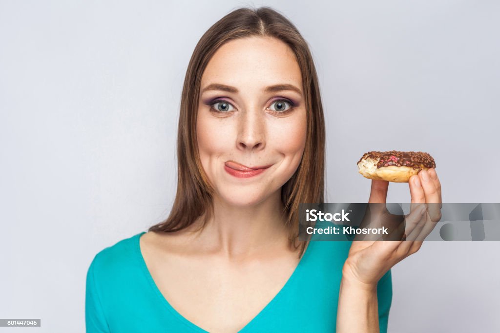 Portrait of beautiful girl with chocolate donuts. Portrait of beautiful girl with chocolate donuts. enjoing and looking at camera with tongue.  studio shot on light gray background. Eating Stock Photo