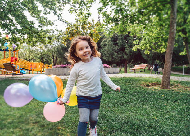 ragazza felice che gioca con un mazzo colorato di palloncini - kids birthday party foto e immagini stock