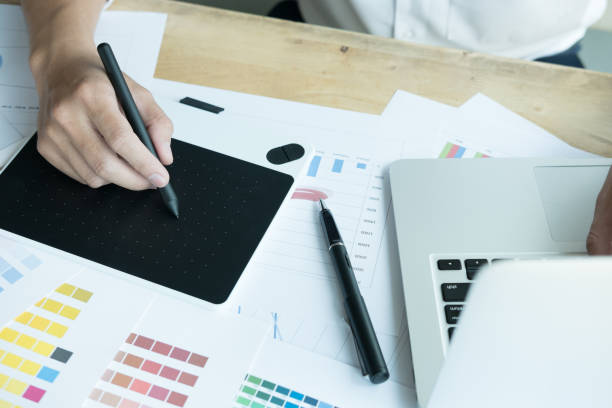 istock young graphic designer working with computer and color swatch. creative man using stylus pen and digital tablet at modern office. Architect using work tools and sample colour catalog. business, technology, design and people concept 801525196