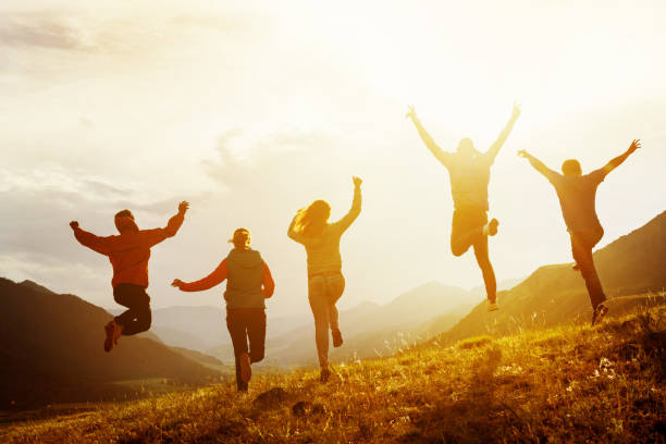 Group of happy friends run and jump Group of five happy friends is running and jumping in sunset light on background of mountains. Happiness and friendship concept jumping stock pictures, royalty-free photos & images